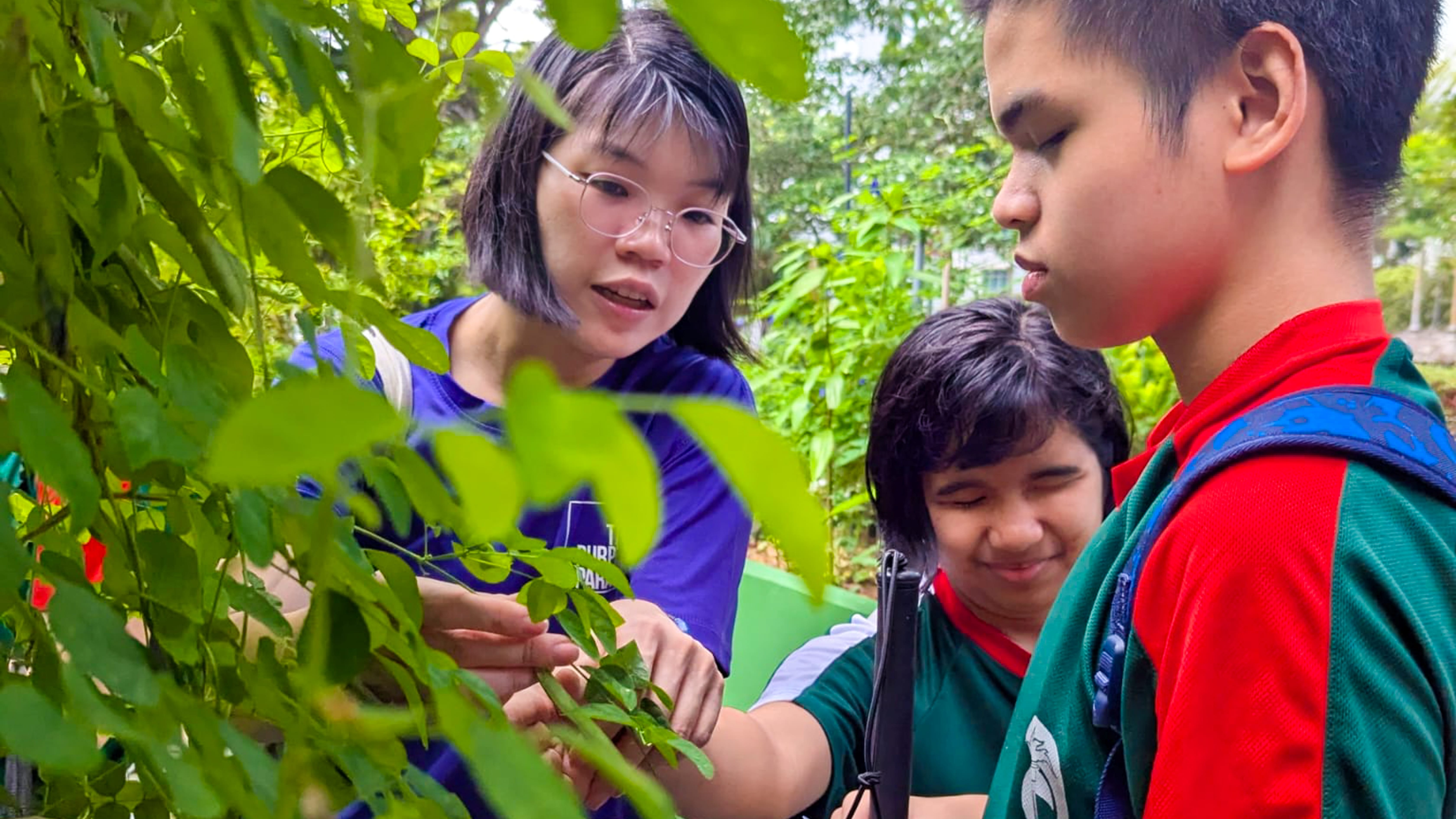 Photo of a teacher helping two VI students in outdoor lesson.